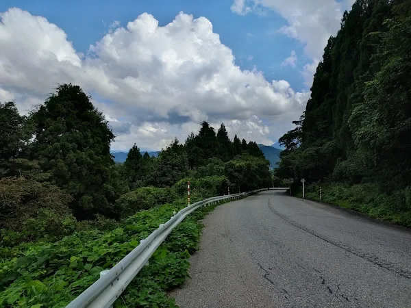 立山町の山間部、緑に囲まれた静かなカーブ道、夏空と白い雲が広がる中を走る
