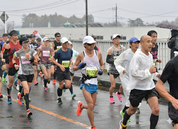 小雨になったつくばマラソン11km以降の様子。レインウェアを着たランナー集団が濡れた路面でも安定したペースで走っている中盤のレース風景
