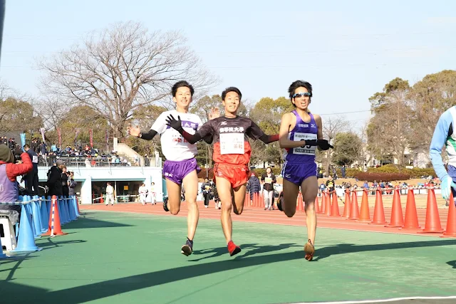 松戸市七草マラソン大会10kmのレース終盤。競技場内で招待選手3名が並んで先頭争いをする様子 - 第28章