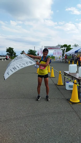 会津磐梯山ウルトラマラソン100kmを完走し、FINISHERフラッグを掲げて笑顔でゴールするバナナぴろし