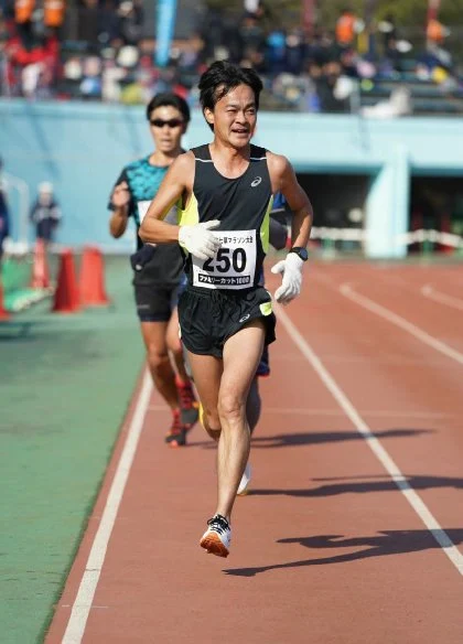 トラック競技場のレース終盤でバナナぴろしが苦しい表情で前傾姿勢で走る市民マラソンの一場面 - 第28章