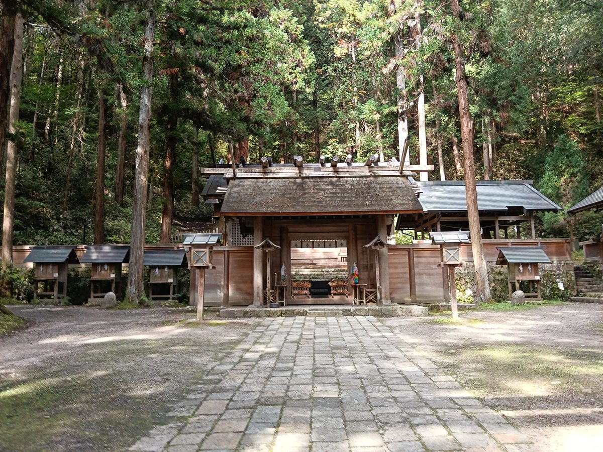 杉木立に囲まれた石畳の参道の先に、檜皮葺の屋根の門が見える