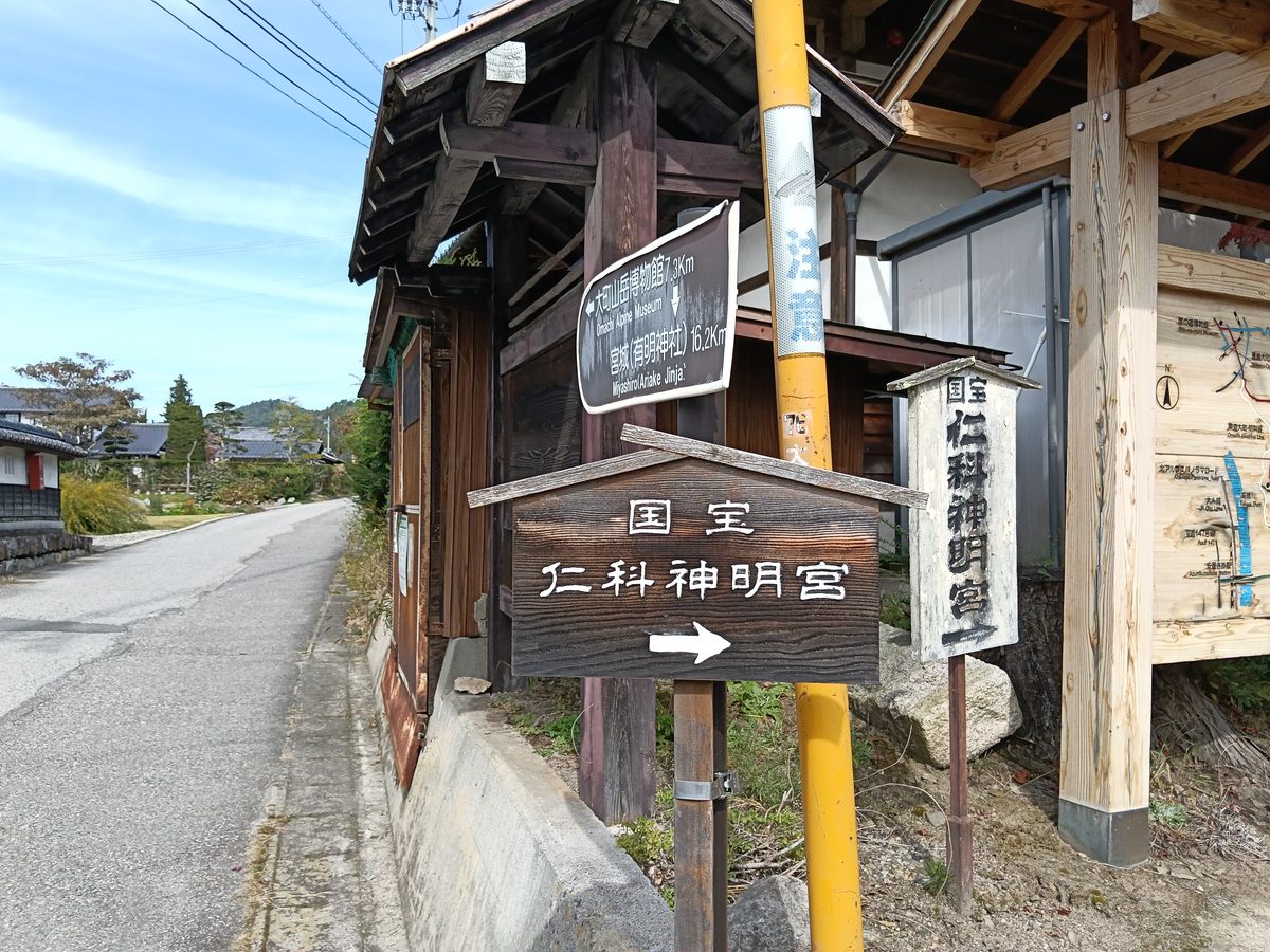道ばたの木の案内板に「国宝 仁科神明宮」と書かれ、矢印が右を指している
